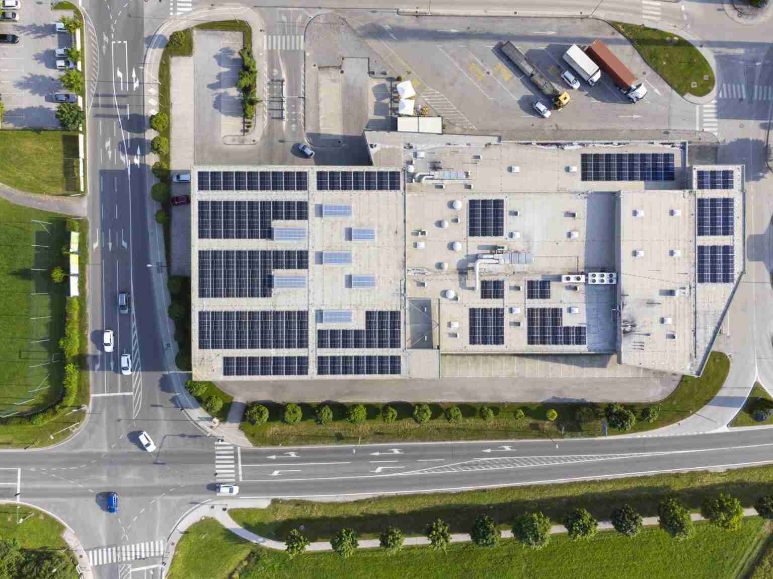 Aerial view of a modern commercial building with solar panels on the roof, and roads with junction and cars, showcasing renewable energy in urban architecture.