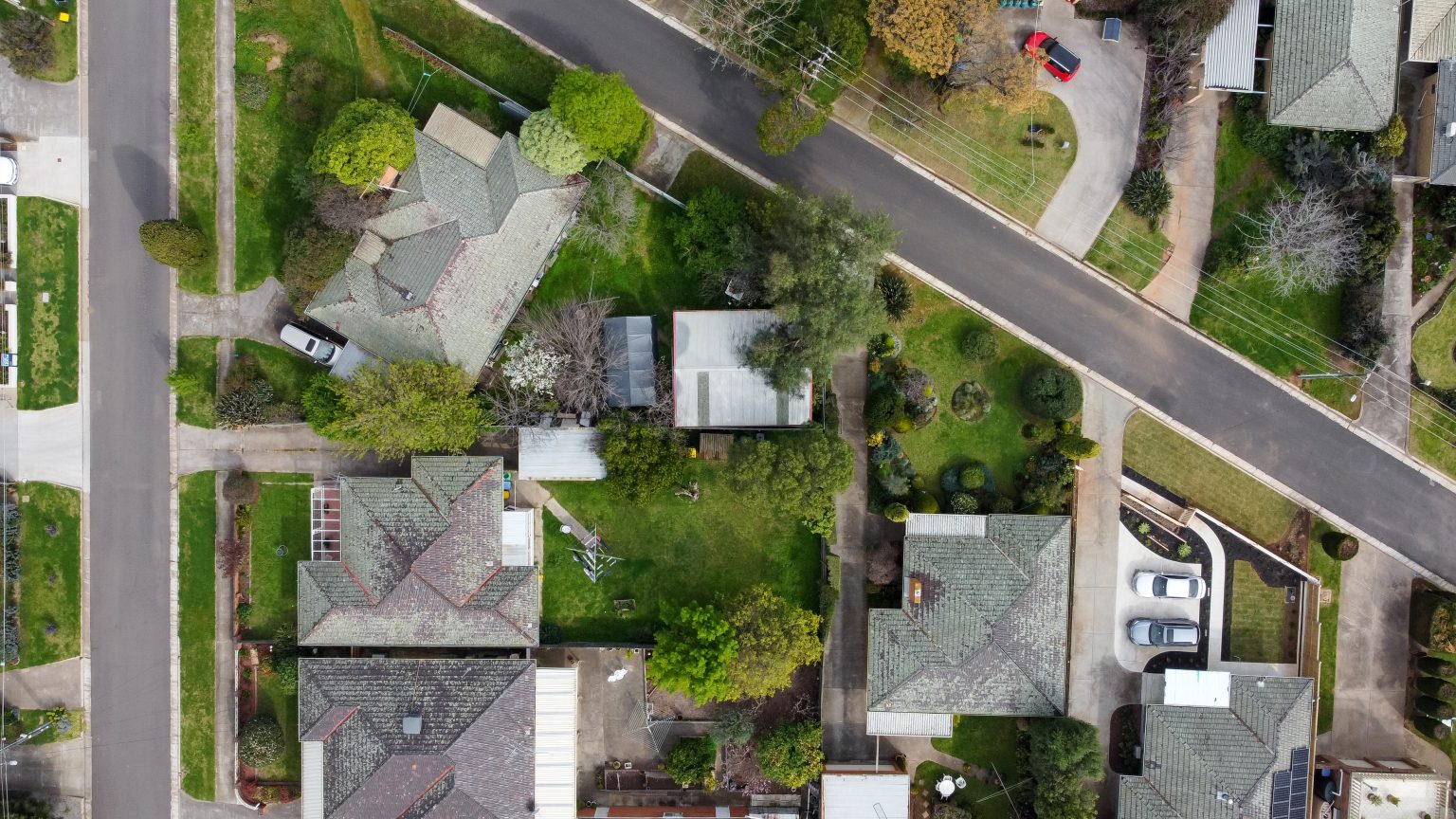 Top down drone view of a small neighborhood of mid-century Australian homes and yards on a quiet street in the outer suburbs of Melbourne